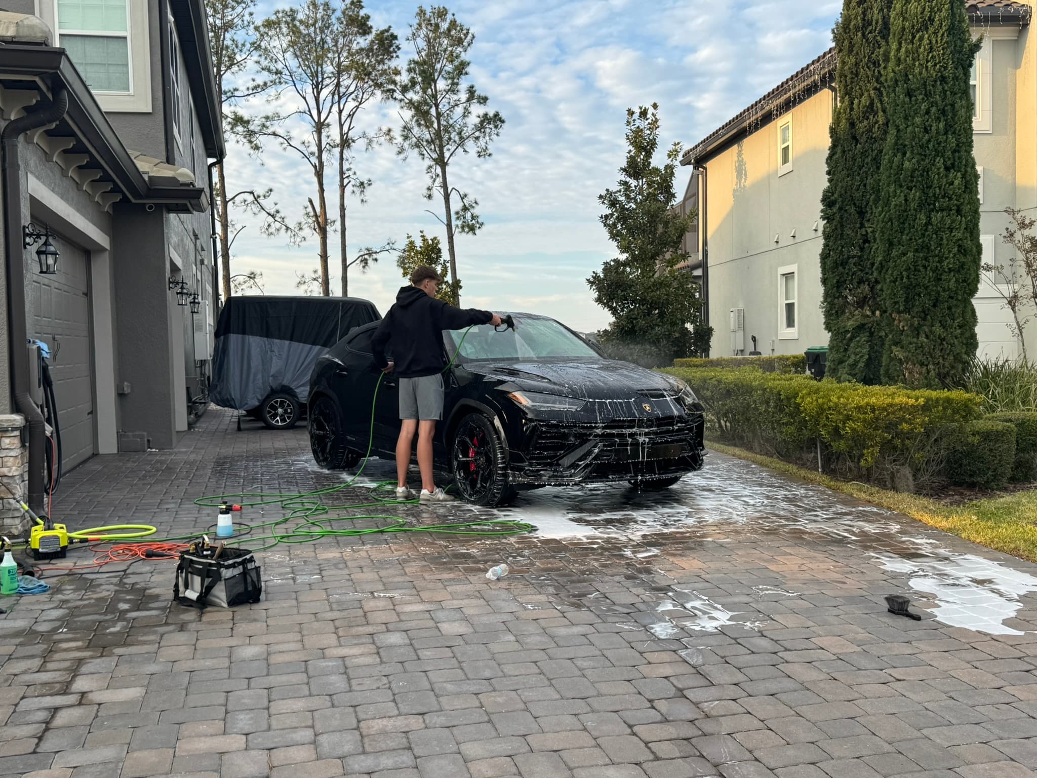Mobile detailer foam-washing a black luxury car in a Central Florida driveway